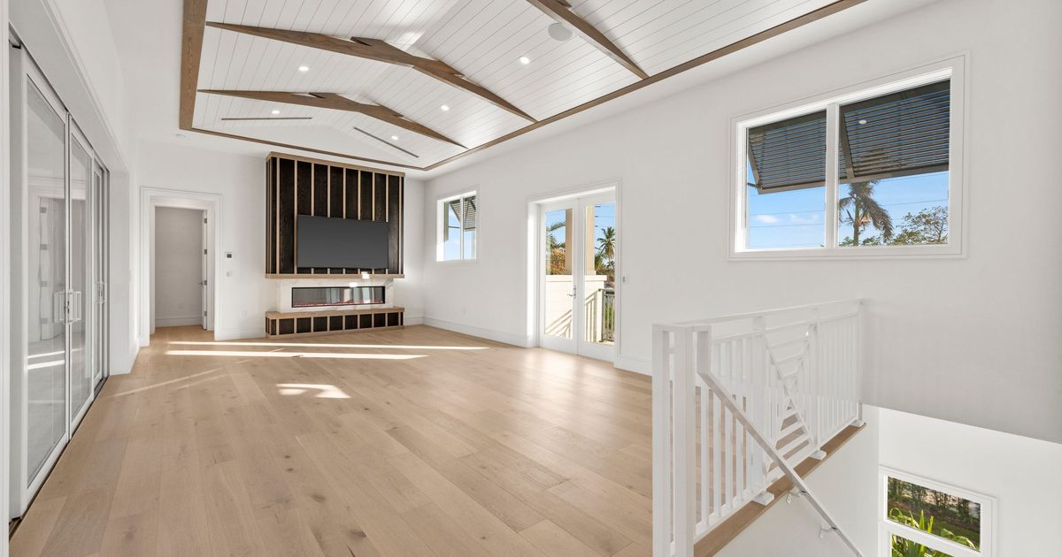 Open upstairs living room with a vaulted wood-trimmed ceiling and a stair opening in a new Naples home.