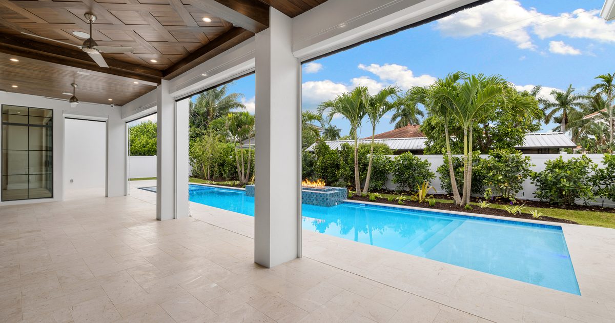 Covered lanai with a wood-paneled ceiling opening onto a pool at a Naples home.