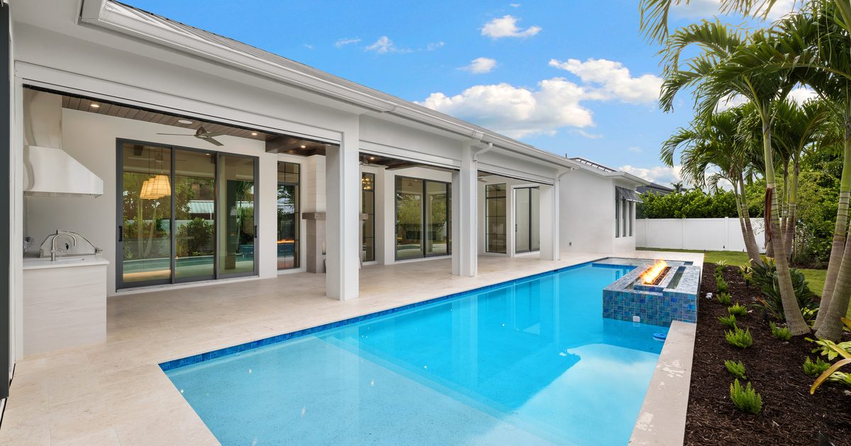 Rectangular pool with a raised fire feature beside a covered lanai at a Naples home.