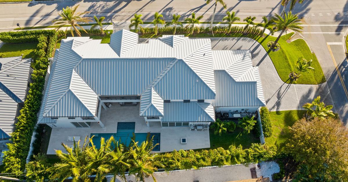 Aerial view of a home’s roof and lot with a pool courtyard, landscaping and the street beside it at a Naples property.