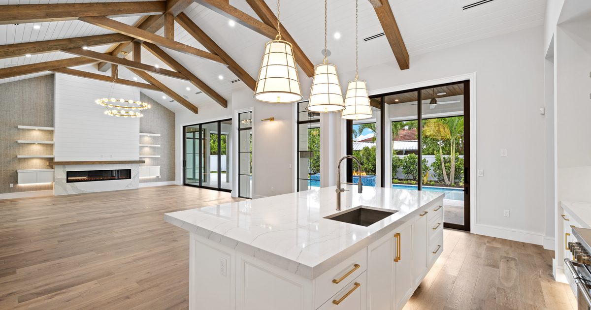 Open great room with exposed timber trusses and a kitchen island in a new Southwest Florida home