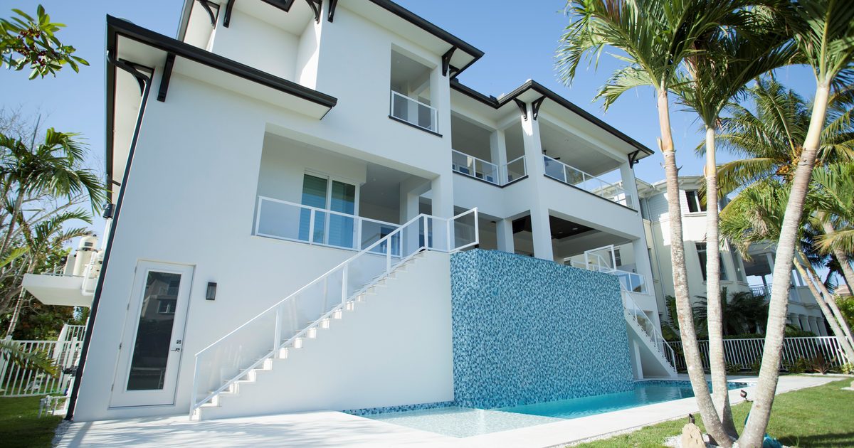 Rear of a three-story waterfront home in Naples with balconies and a tiled pool wall
